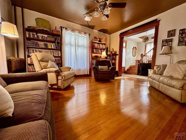 living room with ceiling fan with notable chandelier, stairway, and wood finished floors