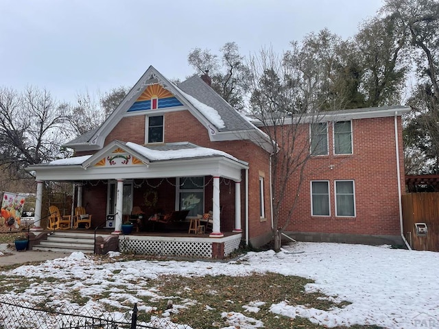 snow covered property featuring a porch, roof with shingles, and brick siding