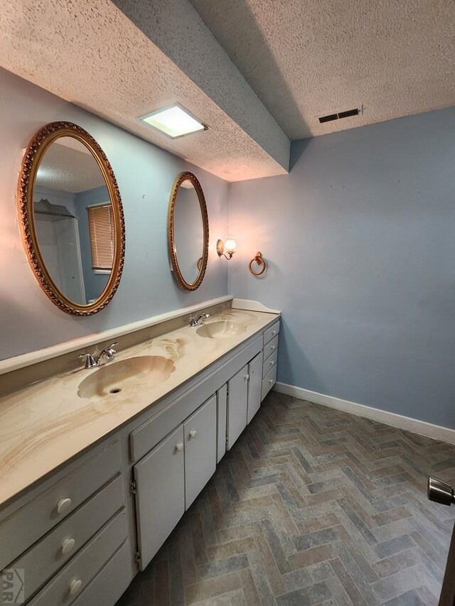 full bathroom featuring a textured ceiling, a sink, visible vents, and baseboards