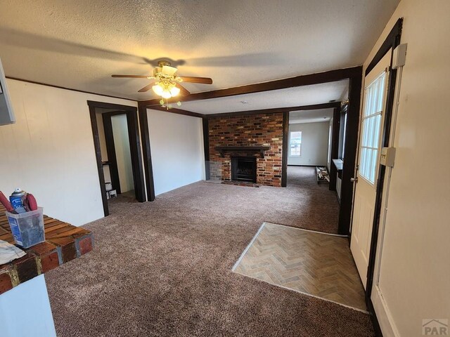 unfurnished living room with a textured ceiling, dark carpet, a fireplace, and a ceiling fan