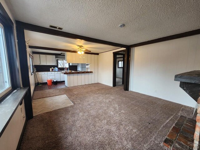 unfurnished living room with dark colored carpet, visible vents, ceiling fan, and a textured ceiling