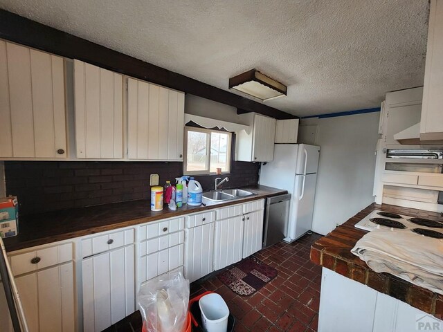 kitchen with stainless steel dishwasher, brick floor, a sink, and white cabinets