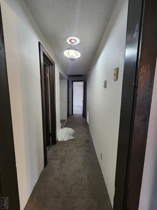 hall featuring a textured ceiling, a textured wall, and dark carpet