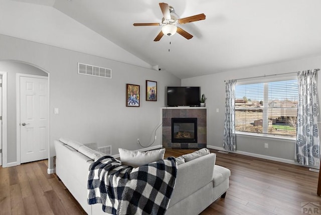 living room featuring arched walkways, vaulted ceiling, wood finished floors, and visible vents