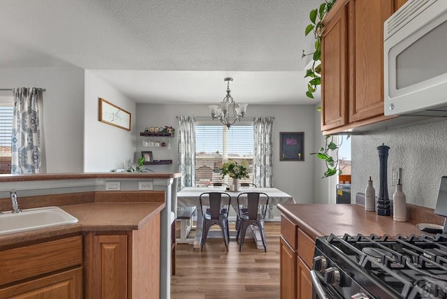 kitchen with a chandelier, brown cabinets, a sink, and white microwave