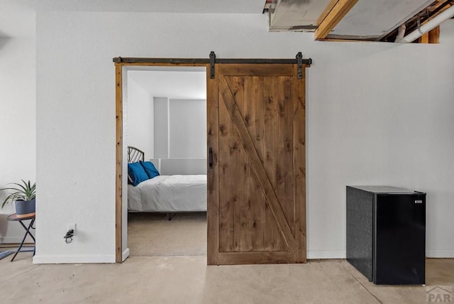 bedroom featuring a barn door, concrete floors, baseboards, and freestanding refrigerator