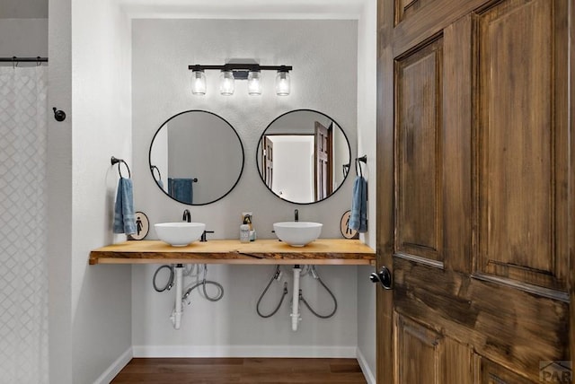 full bath with baseboards, a sink, and wood finished floors