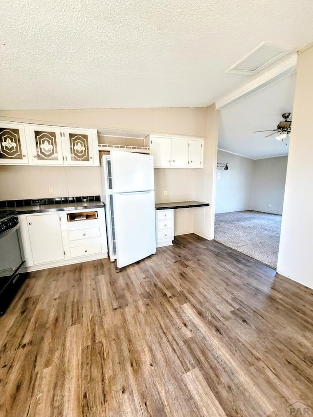 kitchen with dark countertops, lofted ceiling, glass insert cabinets, freestanding refrigerator, and white cabinets