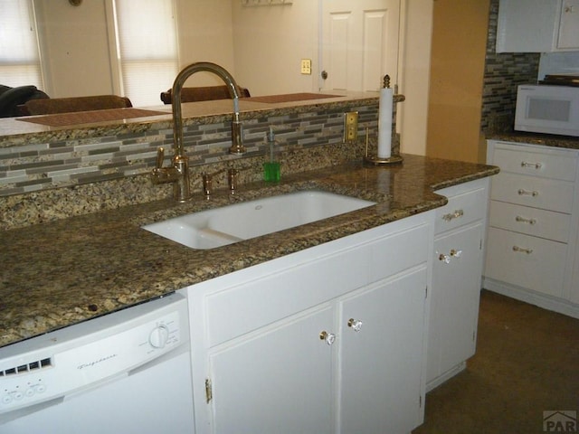 kitchen with tasteful backsplash, a sink, dark stone countertops, white appliances, and white cabinetry