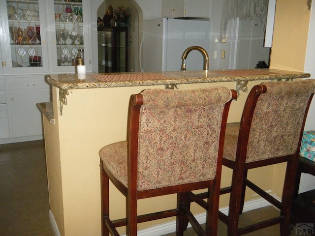 interior space featuring a sink, light stone counters, freestanding refrigerator, and glass insert cabinets