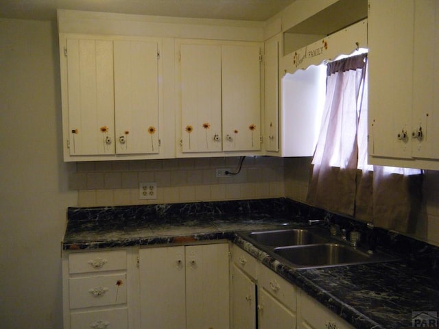 kitchen featuring white cabinets, dark countertops, a sink, and tasteful backsplash