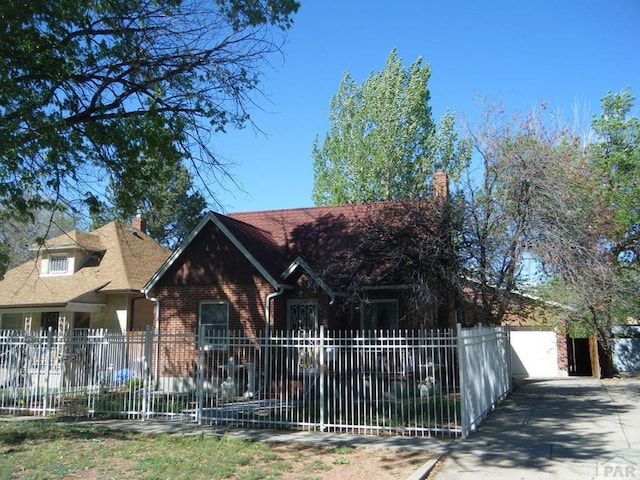 view of front facade featuring fence private yard, brick siding, driveway, and a chimney