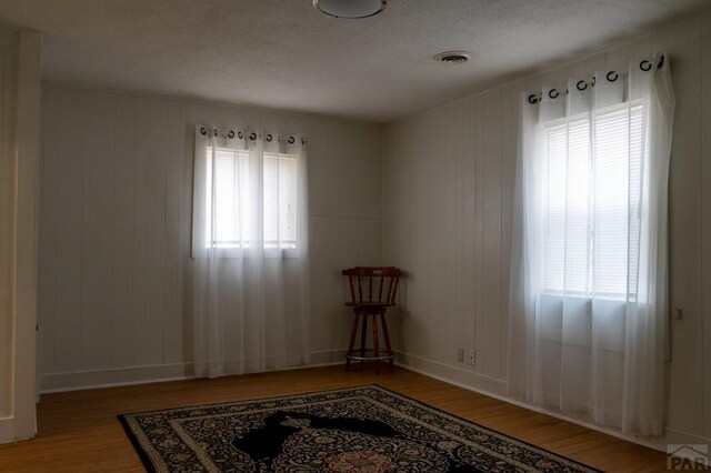 spare room with a wealth of natural light, wood finished floors, visible vents, and baseboards