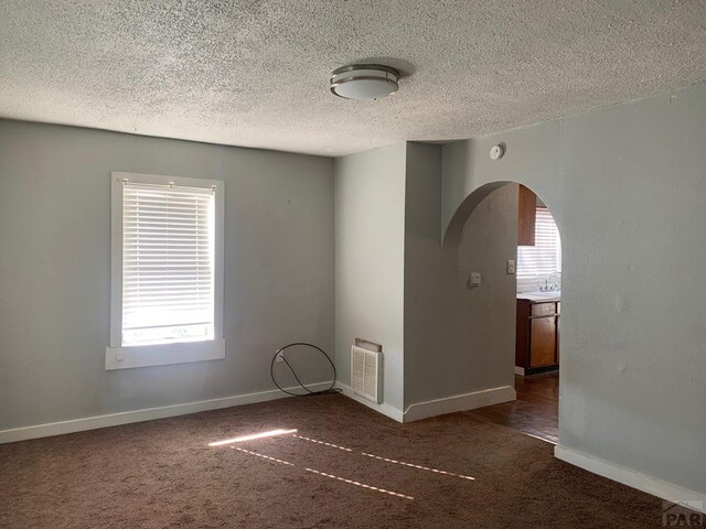 unfurnished room with arched walkways, dark carpet, visible vents, and baseboards