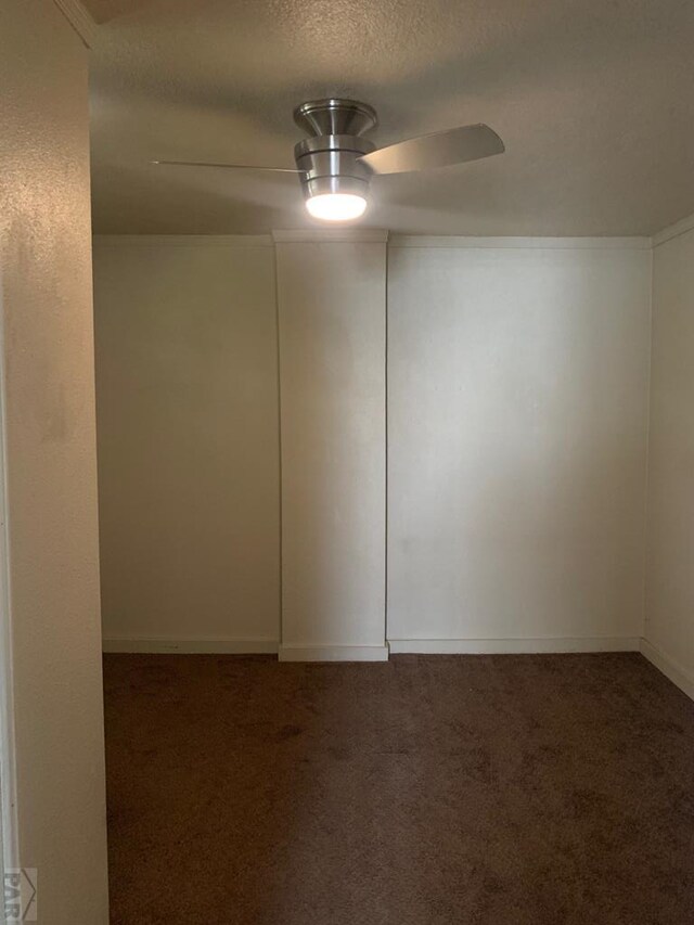 empty room featuring ceiling fan, dark carpet, and a textured ceiling