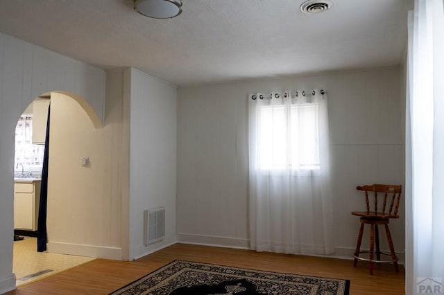 spare room featuring arched walkways, visible vents, and wood finished floors