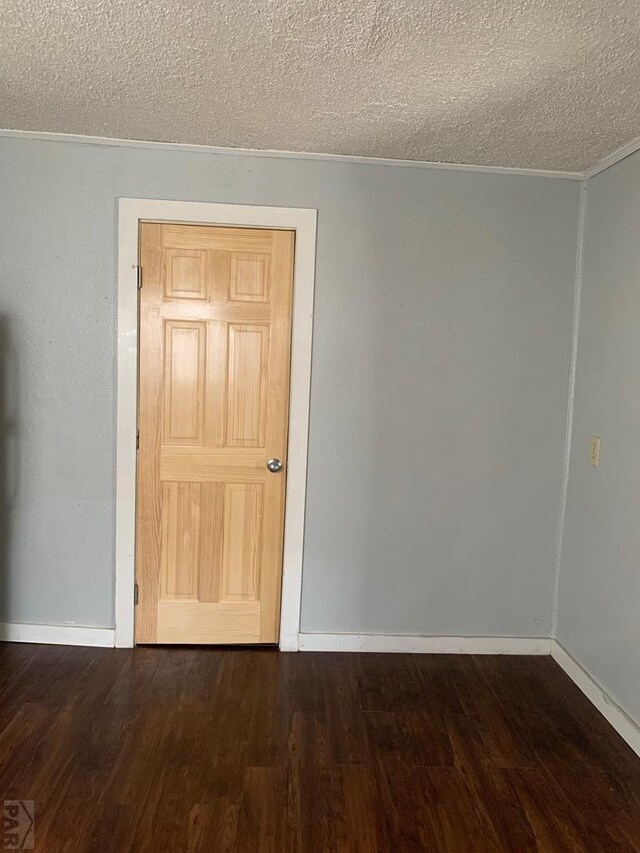 empty room with a textured ceiling, dark wood finished floors, and baseboards