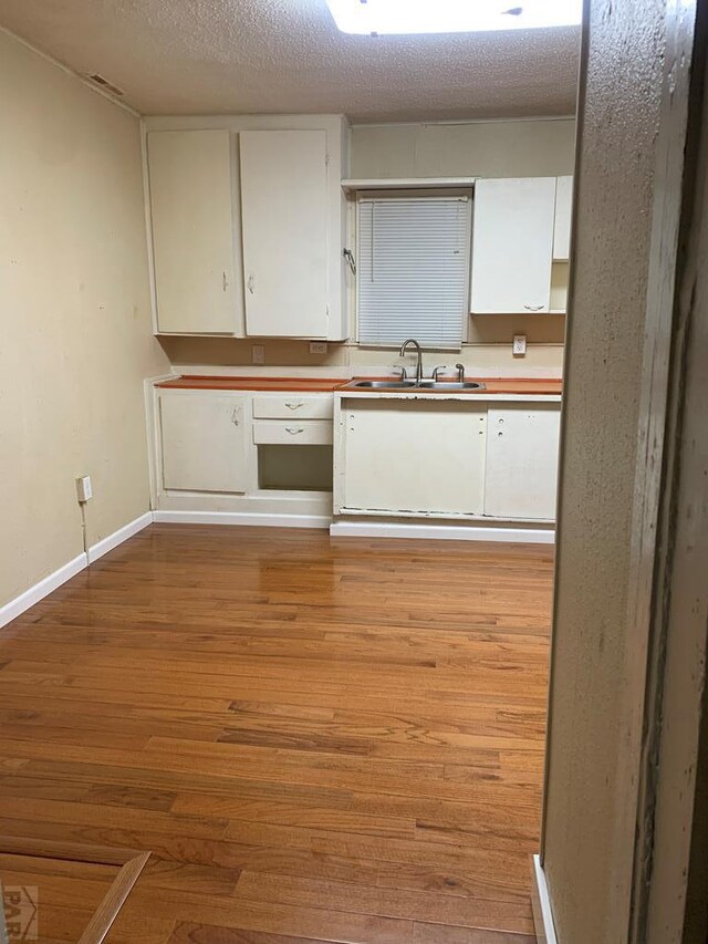 kitchen featuring light wood-style flooring, baseboards, white cabinets, and a sink