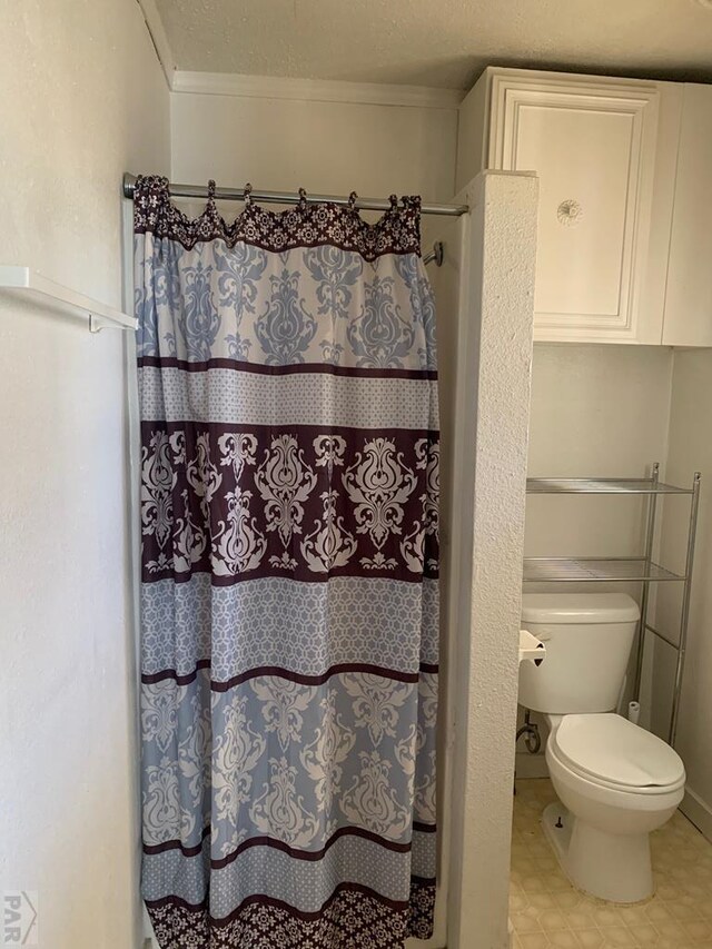 bathroom featuring toilet, curtained shower, a textured ceiling, and tile patterned floors