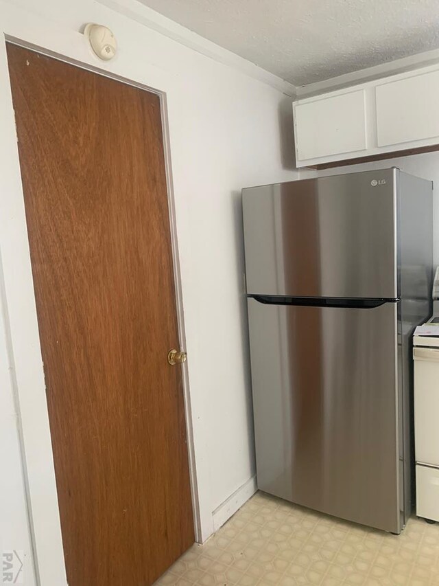 kitchen with light floors, electric range oven, freestanding refrigerator, white cabinets, and a textured ceiling