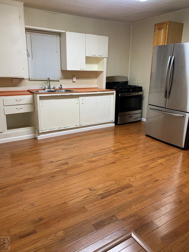 kitchen with stainless steel appliances, white cabinets, a sink, and light wood finished floors