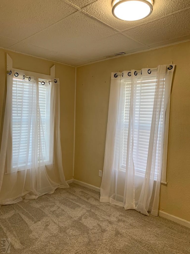 empty room with visible vents, carpet flooring, a drop ceiling, and baseboards