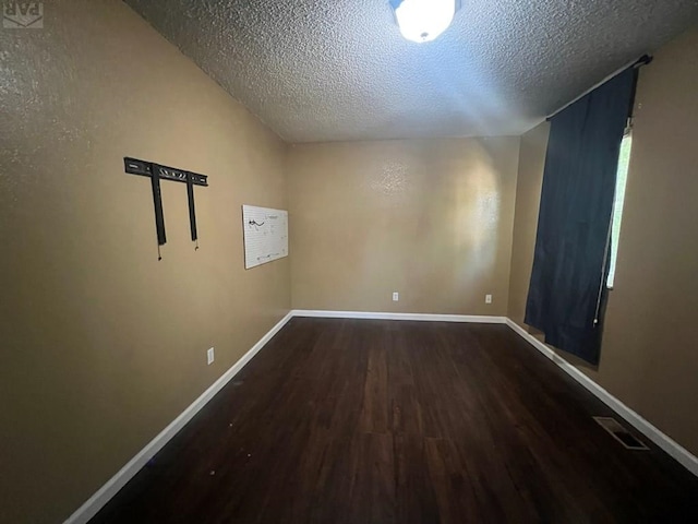 unfurnished room featuring dark wood-type flooring, visible vents, and baseboards