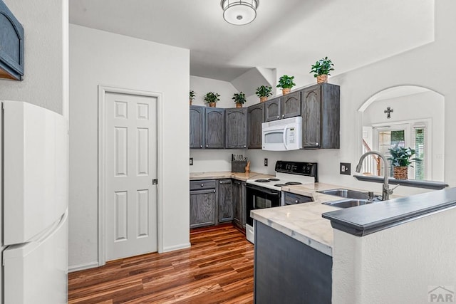 4141 Outlook Blvd Unit Q, Pueblo, CO 81008 - kitchen with white appliances, dark wood-style flooring, a peninsula, arched walkways, and vaulted ceiling