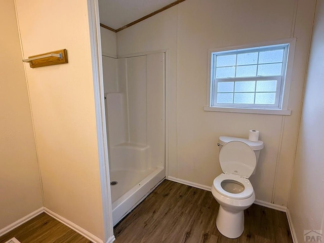bathroom featuring baseboards, wood finished floors, toilet, and a shower
