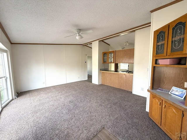 unfurnished living room with a textured ceiling, a ceiling fan, carpet, and ornamental molding
