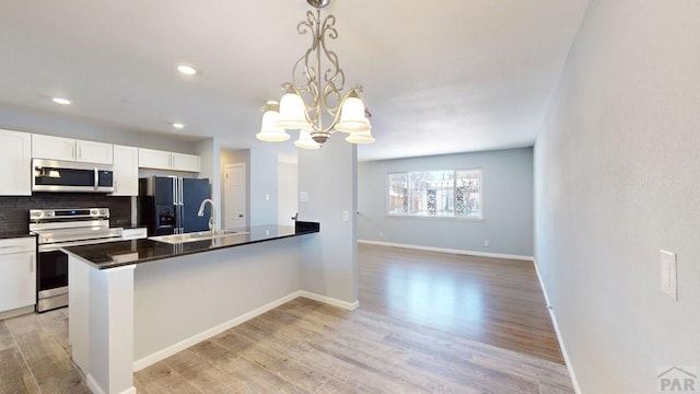 kitchen with appliances with stainless steel finishes, white cabinets, hanging light fixtures, and a sink