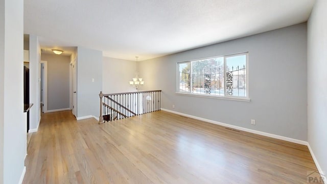 spare room with light wood-style floors, baseboards, and an inviting chandelier