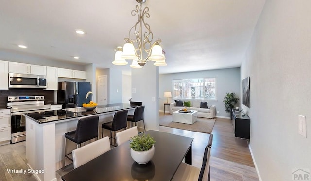 dining area with light wood-type flooring, baseboards, a notable chandelier, and recessed lighting