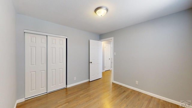 unfurnished bedroom featuring a closet, light wood-type flooring, and baseboards