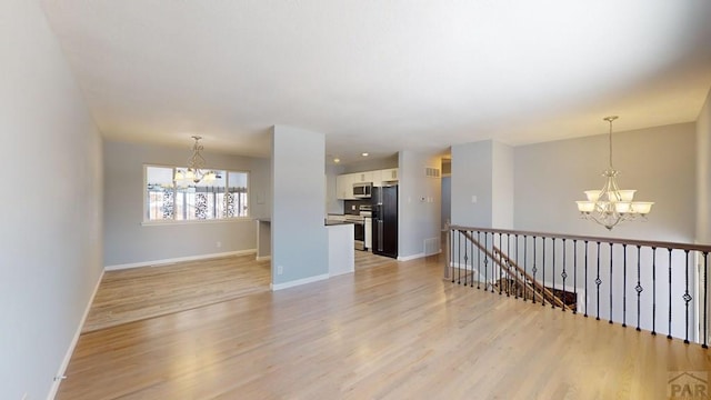 unfurnished room featuring light wood-type flooring, an inviting chandelier, visible vents, and baseboards