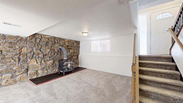 below grade area with a wood stove, stairway, carpet, and visible vents