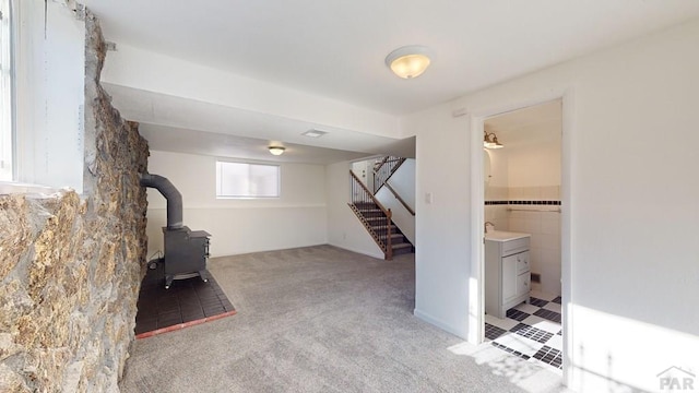 basement featuring a wood stove, light carpet, a sink, and stairway