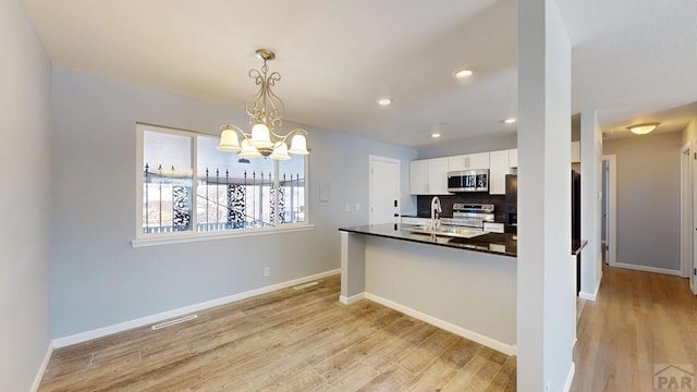 kitchen featuring stainless steel appliances, light wood-style floors, white cabinets, hanging light fixtures, and dark countertops