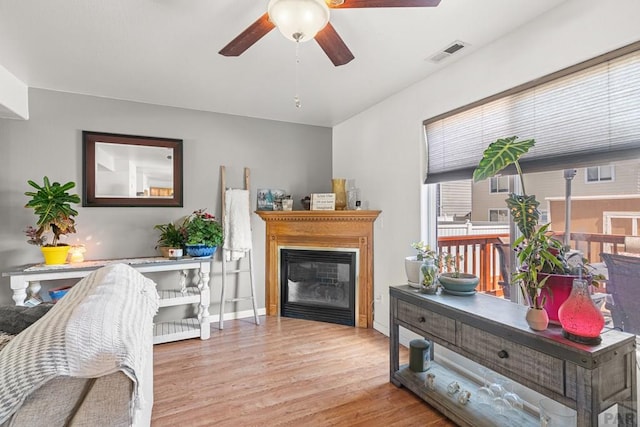 interior space featuring ceiling fan, visible vents, wood finished floors, baseboards, and a glass covered fireplace