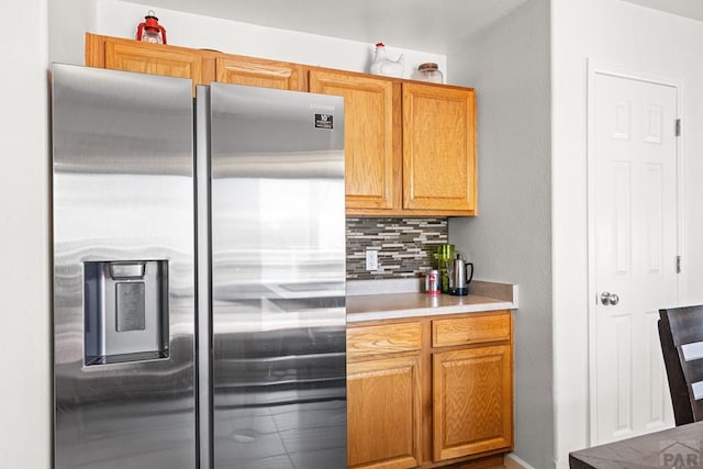 kitchen with light countertops, decorative backsplash, and stainless steel refrigerator with ice dispenser