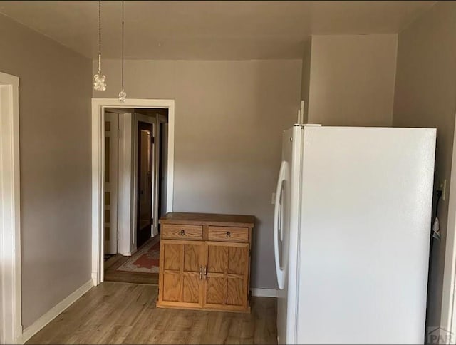 kitchen featuring dark countertops, hanging light fixtures, light wood-style floors, freestanding refrigerator, and baseboards