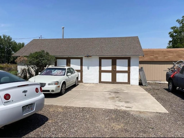 ranch-style house featuring a garage, a shingled roof, concrete driveway, and an outdoor structure