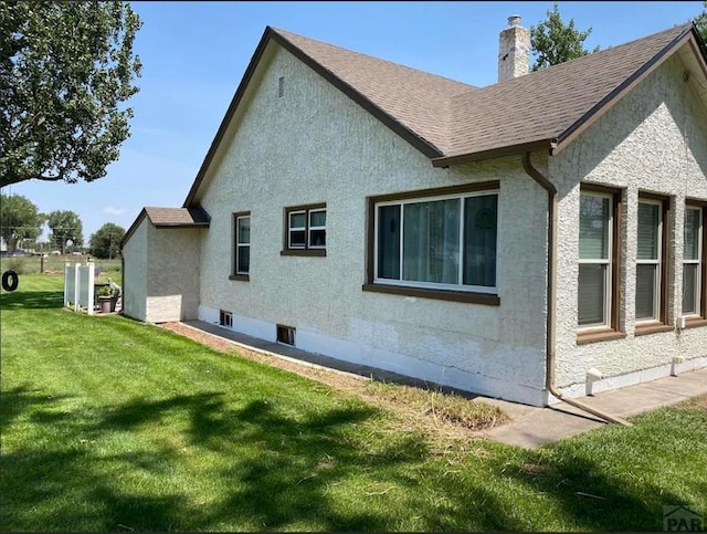 back of property featuring stucco siding, a shingled roof, a chimney, and a yard