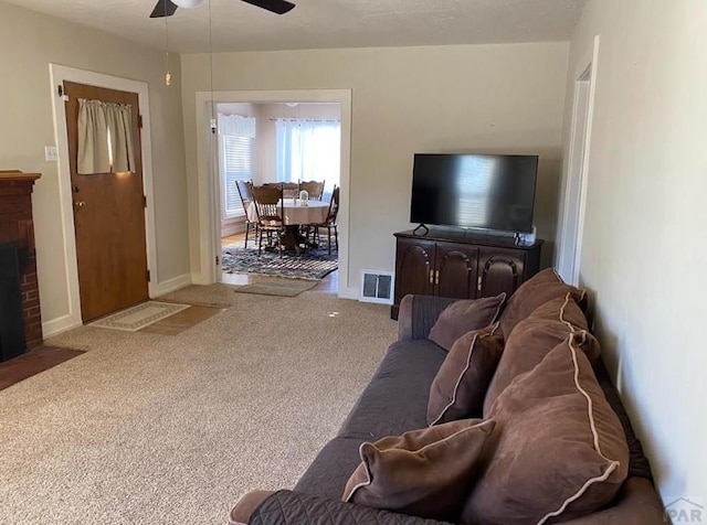 living room featuring carpet floors, visible vents, baseboards, a ceiling fan, and a brick fireplace