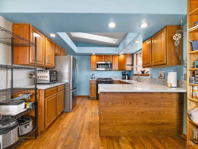 kitchen featuring a peninsula, a tray ceiling, stainless steel appliances, light countertops, and a sink