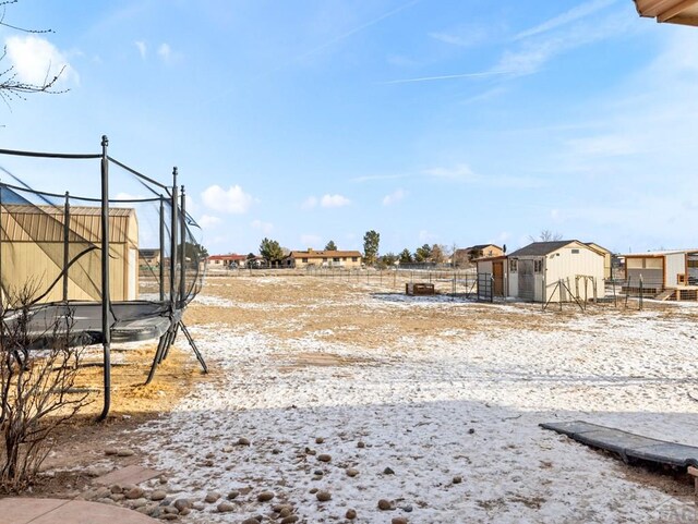 view of yard featuring an outbuilding, a shed, a trampoline, and fence