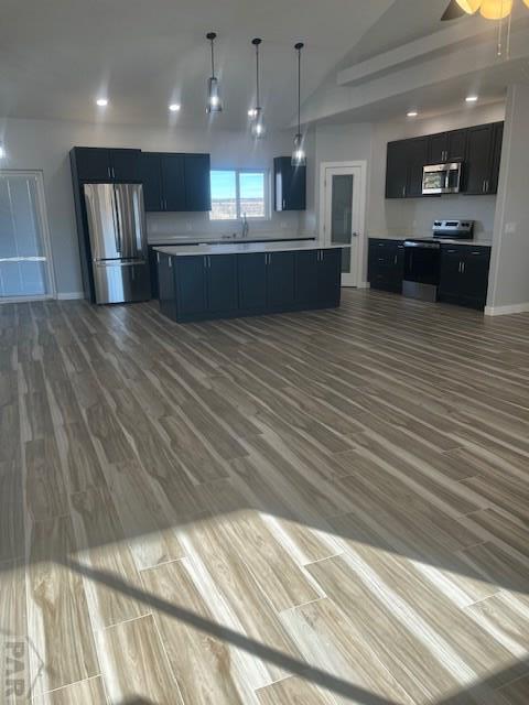 kitchen featuring lofted ceiling, wood finished floors, stainless steel appliances, light countertops, and pendant lighting