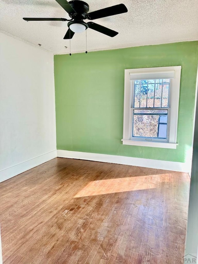 spare room featuring ceiling fan, a textured ceiling, baseboards, and wood finished floors