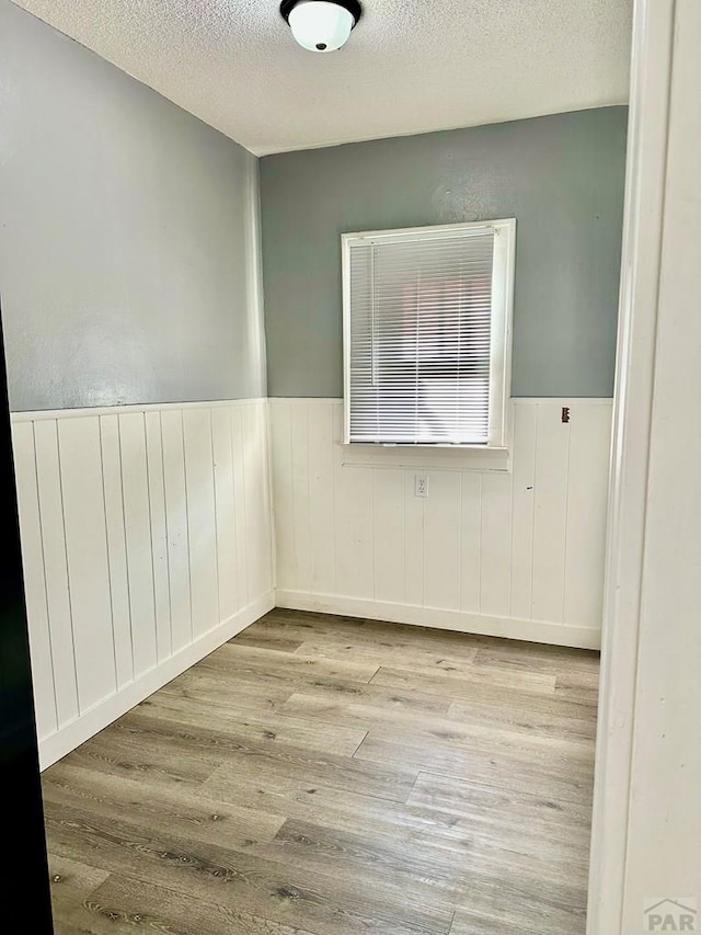 empty room featuring a textured ceiling, light wood finished floors, and wainscoting