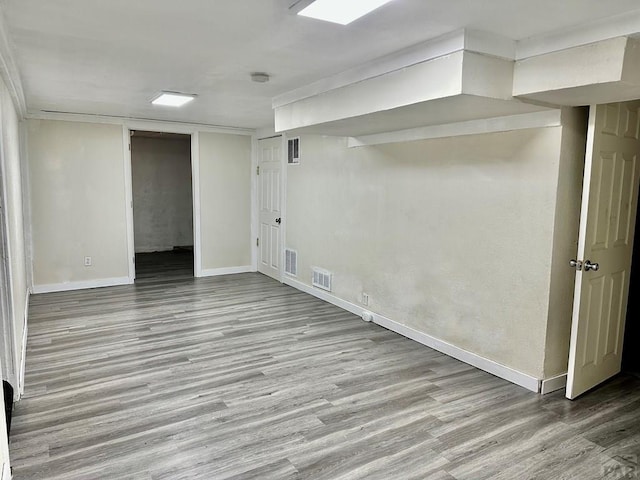 finished basement featuring visible vents, light wood-style flooring, and baseboards